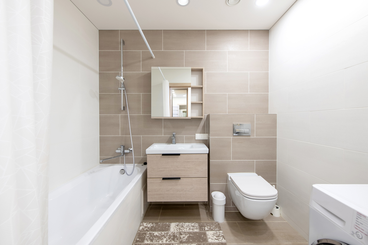 Bright and minimalist bathroom with beige tiles, a wall-mounted sink, a bathtub, and a washing machine. A practical and functional space combining a clean aesthetic with everyday utility.